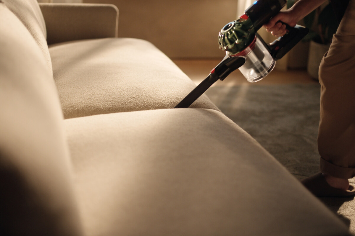 Black and green Dyson V8 Cyclone using its crevice tool between sofa cushions
