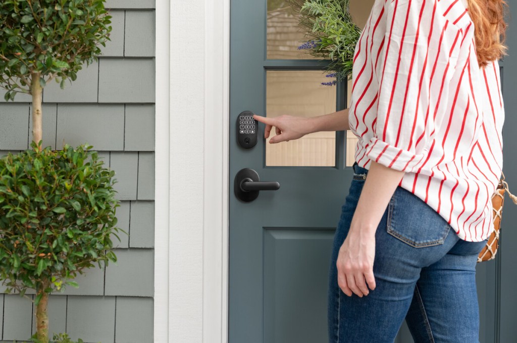 Person pressing the keypad of a Schlage Arrive Remsen deadbolt in Matte Black on a front door