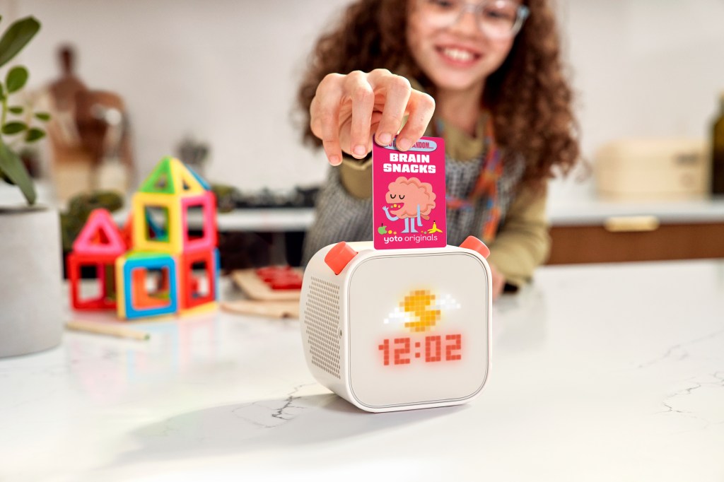 Child inserting a Brain Snacks card into a Yoto Player 3 with orange controls.